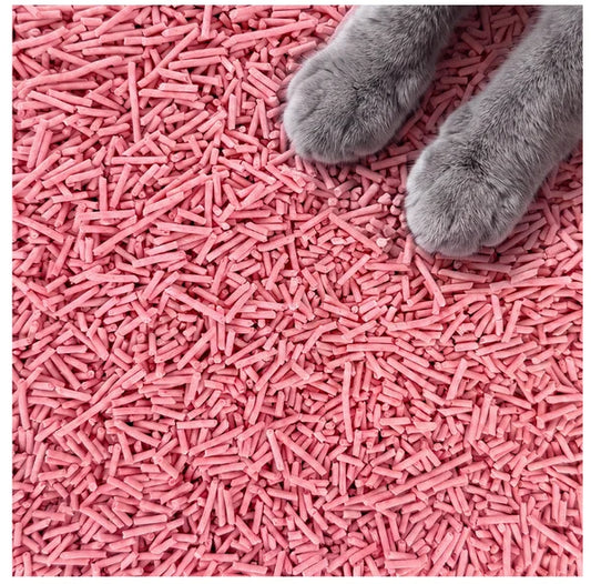 Pink cat litter pellets covering the entire frame, with a gray cat paw entering from the top right corner.