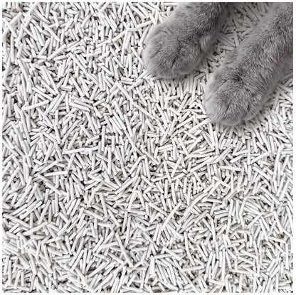 White cat litter pellets covering the entire frame, with a cat's paws visible in the top-right corner.