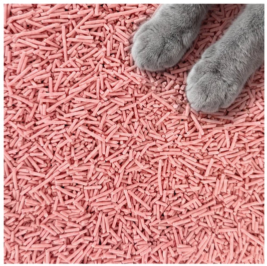 Peach cat litter pellets covering the entire frame, with a gray cat's paws visible in the top-right corner.