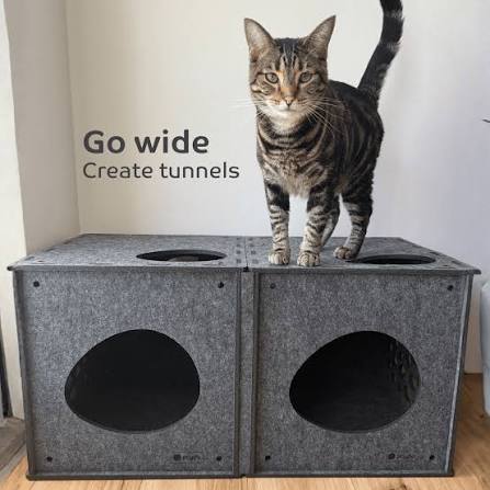 Two gray felt cat tunnels joined together to form a tunnel, with a tabby cat standing on top. Text on the image reads 'Go wide Create tunnels'.